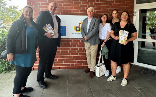 Sechs Menschen stehen vor einem Schild und lächeln. | © Senatskanzlei