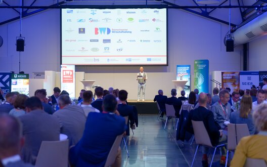 Sponsor:innen, Partner:innen und Gäste lassen sich im Rahmen des Wirtschaftsdialoges 2024 im Fischbahnhof Bremerhaven zu den Themen Digitalisierung, Künstliche Intelligenz und Automatisierung als Treiber der Veränderung inspirieren. Auf dem Bild: Moderator Frank Astor. | © BIS / Schimanke