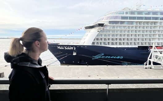 Eine Frau steht am Bremerhavener Kreuzfahrtterminal und schaut auf ein Kreuzfahrtschiff | © Helmut Stapel