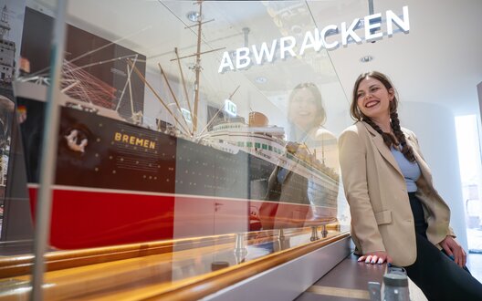 Junge Frau lehnt an einem Schiffsmodell hinter Glas | © WFB/Björn Hake